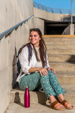 Sırt çantalı neşeli turist kadın merdivenlerde otururken gülümsüyor. Seyahat kavramı.