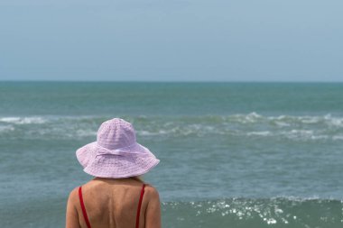 Sahilde güneşli bir günün tadını çıkarırken şapkalı bir kadının denize bakışı. Yaz konsepti.