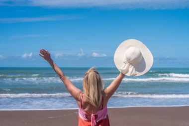 Kumsalda el kaldırırken şapkasını tutan mutlu kadın. Yaz konsepti.