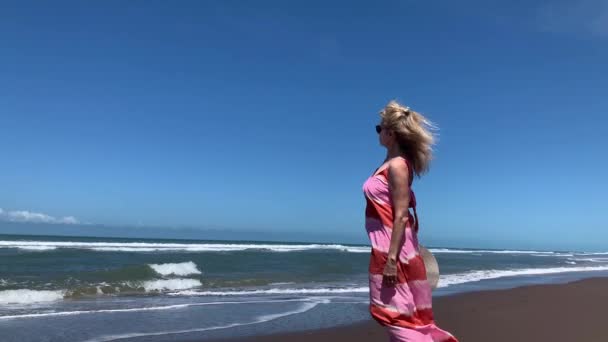 在阳光明媚的夏日里 一个成熟的女人带着微风从海滩上眺望大海 4K镜头 — 图库视频影像