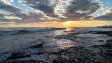 Gün batımında sahilin kayalıklarına vuran deniz dalgalarının görüntüsü. Yaz ve doğa kavramı.