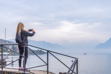 Göl ve dağ manzarasını çekerken elinde cep telefonu olan bir kadın. Seyahat ve teknoloji konsepti.