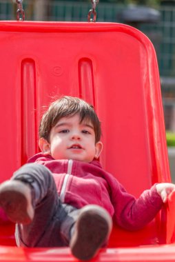 Parktaki oyun parkında sallanan sandalyede eğlenen küçük çocuk. Çocukluk kavramı.