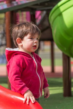 Parktaki oyun parkında kaydırağın yanında dururken kafası karışmış bir şekilde yüzünü çeviren küçük çocuk. Çocukluk kavramı.
