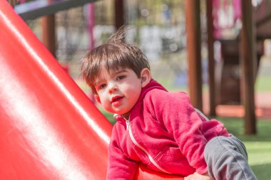 Küçük çocuk oyun parkında oynarken kaydırağa tırmanıyor. Çocukluk kavramı.