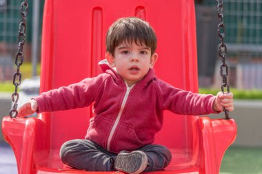 Küçük çocuk dışarıda parkta salıncakta sallanırken kameraya bakıyor. Çocukluk kavramı.