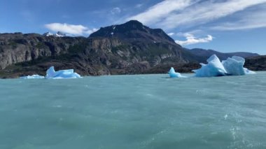 Lago Argentino 'da üzerinde birkaç büyük buz bloğu yüzen büyük bir su kütlesi. Su mavi ve gökyüzü berrak.