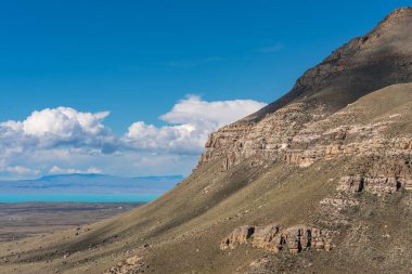 Patagonya bozkırında mavi gökyüzü ve arkasında Lago Argentino olan bir dağ. Dağ çimen ve taşlarla kaplı.