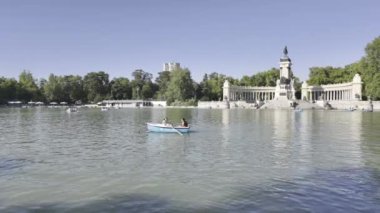 Madrid, İspanya 'daki Retiro Park' taki Alfonso XII Anıtı 'nın manzarası güneşli bir günde insanların gölde kayıkla gezmelerinin keyfini çıkarıyor.. 