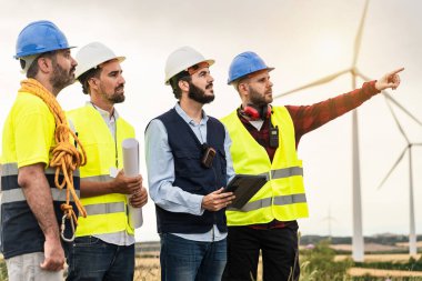 Yel değirmeni elektrik santralinin önünde çalışan profesyonel işçiler. İnşaat mühendisi ve elektrikçilerin projeler hakkında tartışmalarının arka planı