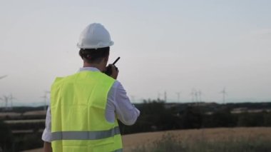 Rüzgar türbininin güç istasyonunda yürüyen ve telsiz kullanan bir işçi. Kask takan mühendis ve elektrik altyapısını inceleyen sarı mühendis.