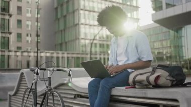 İnternetteki son moda Afrikalı Amerikalı adam dizüstü bilgisayar kullanıyor, dışarıda klasik bisikletin yanında oturuyor.