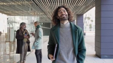 Kendine güvenen, kendine güvenen, uzun saçlı profesyonel bir adam dışarıda ofis alanında dizüstü bilgisayarla dolaşıyor. İlham verici pazarlama yaratıcı işçiler