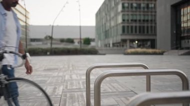 Bisikletle işe gelen Afrikalı Amerikalı adam, bisikleti iş yerinin yakınına park ediyor.