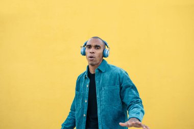 Genç Afrikalı Amerikalı adam kablosuz mavi kulaklıkla müzik dinlemekten hoşlanıyor.