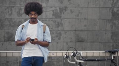 Akıllı telefon kullanan bisikletli genç Afrikalı Amerikalı adam.