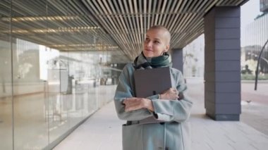 Saçı tıraşlı, kendine güveni tam profesyonel bir kadın dışarıda ofis alanında dizüstü bilgisayarla yürüyor. Reklam reklamcılığından ilham alan yaratıcı iş kadını.