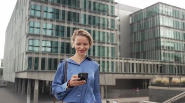 Profesyonel bir kadın ofisin dışında yürürken cep telefonunu kontrol ediyor.
