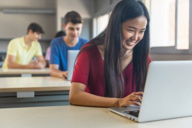 Asyalı bayan üniversite öğrencisi dizüstü bilgisayarla çalışıyor. Lisede ödev yapıyor.