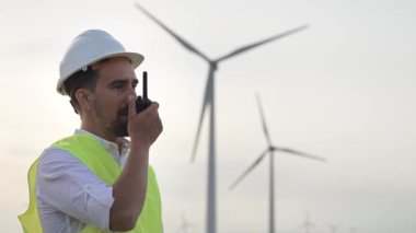 Yel değirmeni güç alanında telsiz kullanan teknik mühendis. Kasklı ve sarı yelekli işçiler telsizle konuşuyor. 