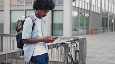 Bisikletli Afrikalı Amerikalı adam şehirde akıllı telefon kullanıyor.