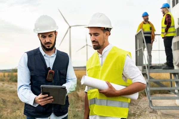 Team of Electrical Technicians and Engineers working in Wind Turbine Electricity Power Station, using tablet to do technical inspection