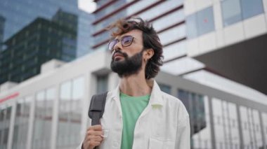Man carrying side bag walking in city near office buildings, looking around in the city