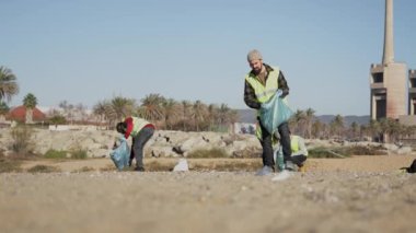 Man cleaning up the beach together with volunteers collecting industrial plastic waste on the coast line 