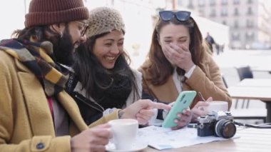 Tourist friends sitting together using mobile phone to share funny content in winter vacations