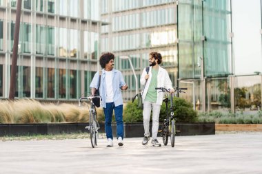Two young adults walking together on the way to work. Young healthy friends with bikes going to the office 