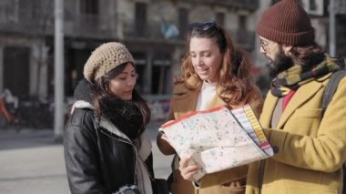 Cheerful young friends looking at smart phone and checking city map direction during winter vacations 