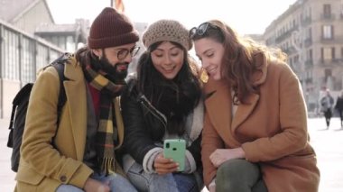 Group of friends sitting together using mobile phone to share content on social media in winter 