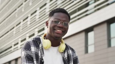 Portrait Of Positive African American Man wearing eyeglasses and yellow headphones Smiling in the city