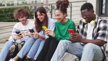 University Students sitting in stairway typing on smartphones - Multicultural group of friends using cell phones 