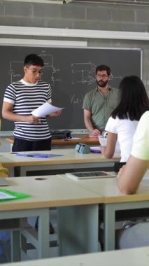 Latin American college student presenting a project reading a composition to classmates and teacher at High School classroom - Vertical Video