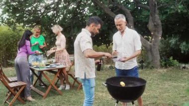 İki yetişkin arkadaş barbekü pişirir ve bira içer bahçe yemeği hazırlar.