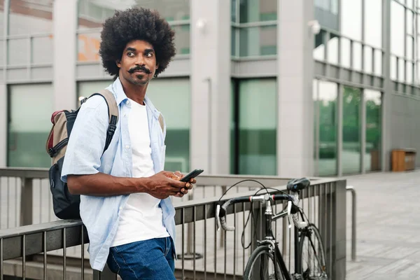 Nuori Afroamerikkalainen Mies Käyttää Matkapuhelinta Polkupyörän Vieressä Katsoen Sivulle — kuvapankkivalokuva