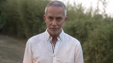 Bahçede gülümseyen kendine güvenen olgun bir adamın portresi.