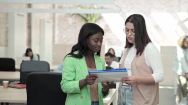Çok ırklı iş kadınlarından oluşan bir ekip birlikte çalışarak yaratıcı şirketin ofisinde proje fikirlerini tartışıyor.