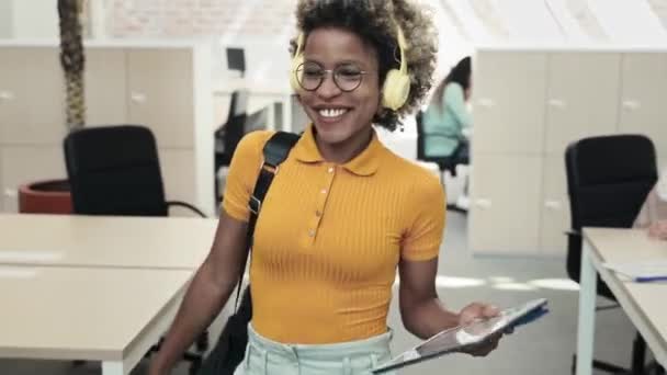 幸せなアフリカ系アメリカ人の流行の女性ヘッドフォンで音楽を聴く休暇や週末にビジネスオフィスを離れる — ストック動画