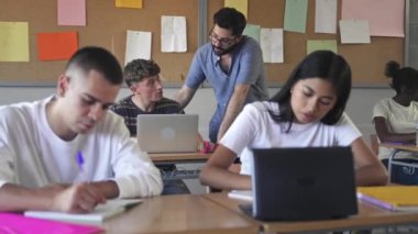 Genç öğretmen, Avrupa 'da lisede öğrencilere laptopla öğrenme konusunda yardım ediyor.