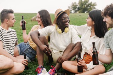 Bir grup genç arkadaş çimenlerin üzerinde oturuyor, yaz festivalinde eğleniyor ve eğleniyorlar. 