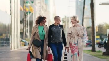 Üç mutlu bayan arkadaş alışveriş torbalarıyla şehirde bahar satışları için yürüyorlar.