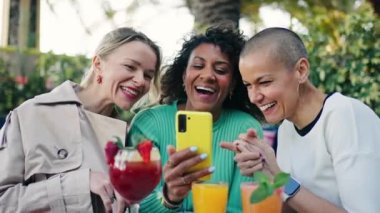Barda içki içerken sosyal medyada komik şeyler izleyen üç mutlu bayan arkadaş.
