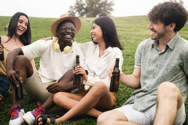 Group of young happy friends sitting on the grass having good times talking and laughing in summer