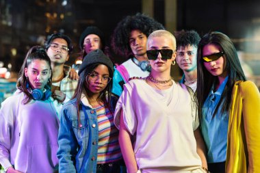 Modern funky tarzı modaya uygun bir grup arkadaş gece vakti şehirde kameraya bakıyorlar.