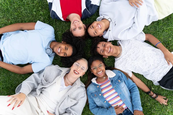 Group of happy young college student friends having fun on the grass together smiling looking to the camera