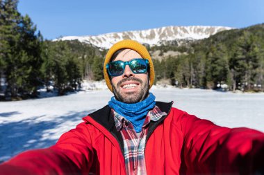 Kızıl kışlık elbiseli genç adam kar ormanlarında selfie çekiyor. 