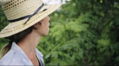 Hasır şapkalı sarışın kadın yemyeşil tarım tarlasında yürüyor.