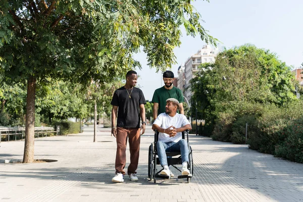 Man in wheelchair with young friends hanging out in the city park - society inclusion diversity